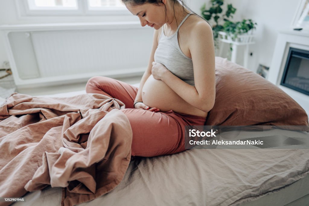 Good morning my sweet baby Photo of a young expectant mother stroking her baby bump and enjoying her morning in the bedroom of her apartment; the daily routine of a pregnant woman. Pregnant Stock Photo