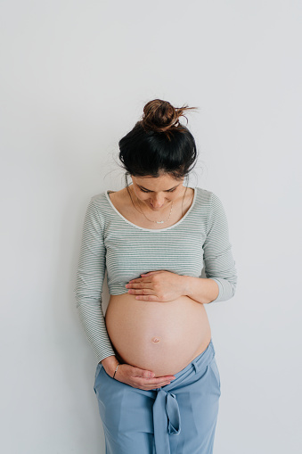 Portrait of a smiling pregnant woman and her growing belly isolated on a white background; daydreaming about her future child.