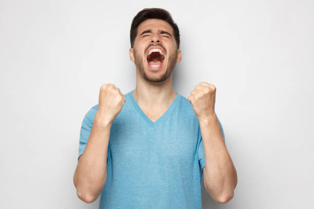 istock Young man shouting with closed eyes, celebrating victory, squeezing fists in deep emotional expression of happiness and luck, isolated on gray background 1252905156