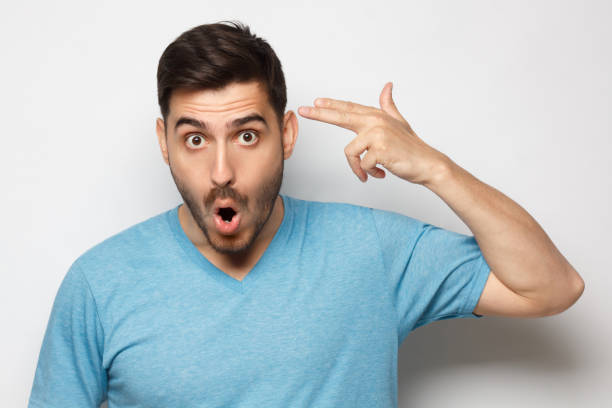 istock Young man pretending committing suicide with finger gun gesture like shooting himself, isolated on gray background 1252905175