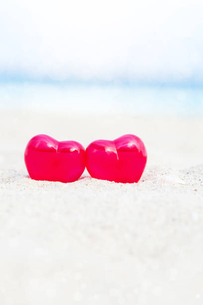 Red decoration hearts on sandy beach with sea background,  shallow depth. Valentines day card and love to travel concept
