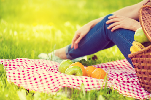 Woman sitting on grass, vegan picnic on red checkered tablecloth with fruits on grass with healthy food in park outside at summer day