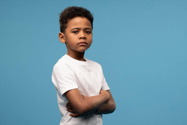 Serious or offended cute little boyin white t-shirt crossing his arms on chest Serious or offended cute little boyin white t-shirt crossing his arms on chest while standing in front of camera over blue background critical thinking kids stock pictures, royalty-free photos & images