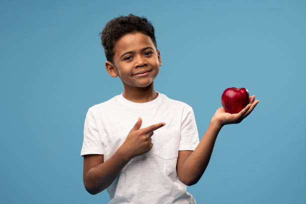 feliz niño africano con gran manzana roja madura en la mano apuntando a la fruta - apple healthy eating eating black fotografías e imágenes de stock