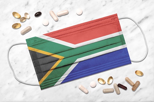 Face mask showing colors of the flag of South Africa during coronavirus pandemic surrounded by pills