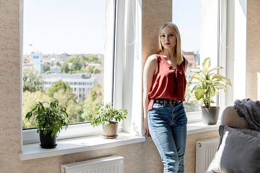young blonde girl stands at a large window in a bright room