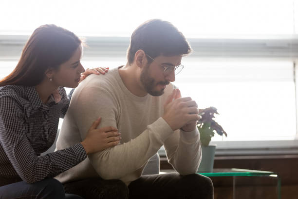 Couple sit on sofa caring wife hugs disappointed sad frustrated husband Couple sit on sofa caring wife hugs disappointed sad frustrated husband, making peace, reconcile after fight, problems in relationship, friendship and support spouses overcome problem together concept edgy man stock pictures, royalty-free photos & images