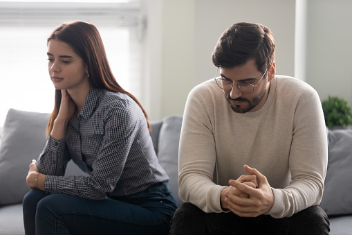 Young couple lost in sad thoughts sitting together on couch thinking feels troubled about problems in relationships, unwanted unexpected pregnancy and difficult decision, break up and divorce concept