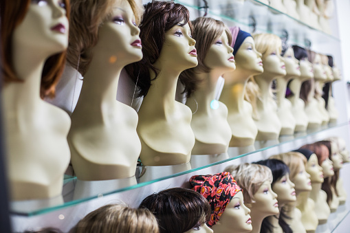 Rows of hair wigs on display, on some dummies, in a store.