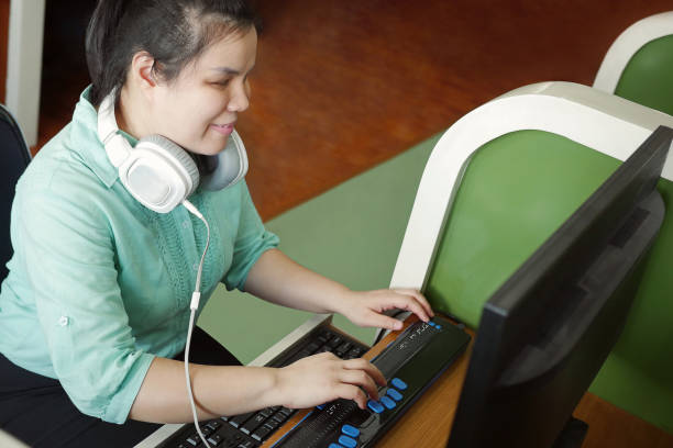 asiatische junge blinde frau mit kopfhörer mit computer mit aktemmbarem braille-display oder braille-terminal ein technologiegerät für menschen mit sehbehinderungen. - zugang stock-fotos und bilder