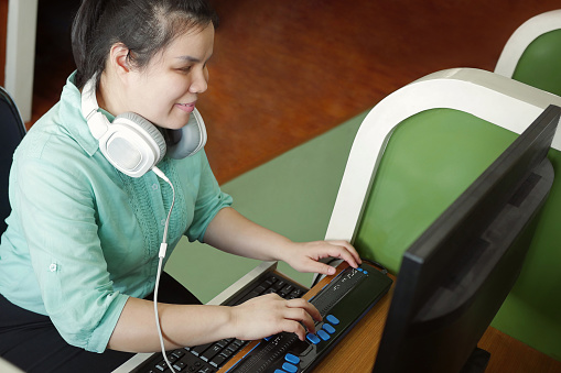 Joven ciega asiática con auriculares utilizando computadora con pantalla braille actualizable o terminal braille un dispositivo tecnológico para personas con discapacidades visuales. photo