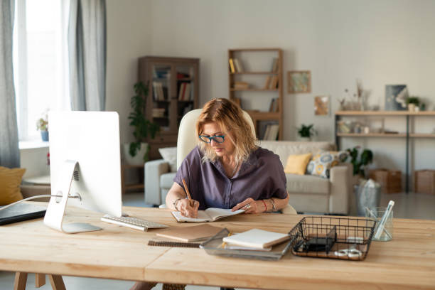 istock Busy mature female in eyeglasses and casualwear writing down working plan points 1252929646
