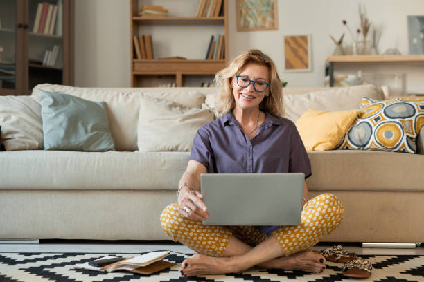 istock Happy mature cross-legged female holding laptop while looking at its display 1252929702