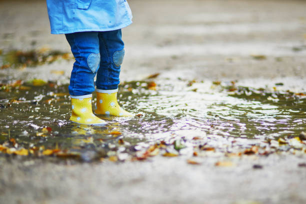 istock Child wearing yellow rain boots and jumping in puddle on a fall day 1252936677
