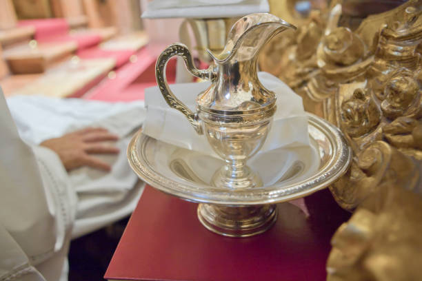 Liturgical wash basin and pitcher beside a sitting priest. Jug and handle decorated with relief elements