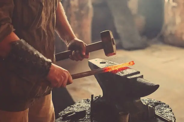 Manual work of a blacksmith in a blacksmith Shop. Hammer blows on the iron billet on the anvil. Forging sword blades is a retro weapon.
