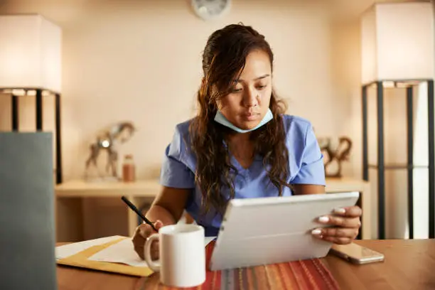 filipina nurse working from home doing paperwork and using tablet on table