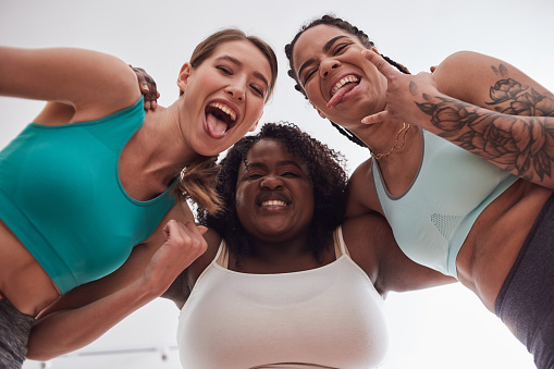 Low angle portrait of three cute laughing young females of different ethnic groups embracing and grimacing close together