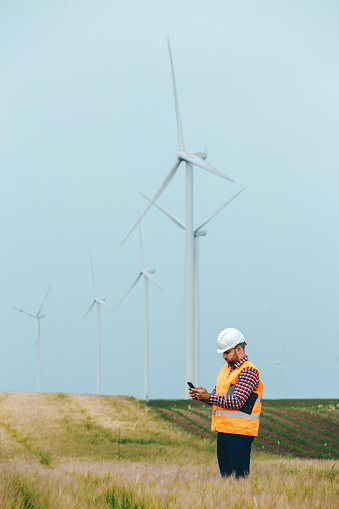 young male engineer holding laptop computer planning and working for the energy industry and standing beside a wind turbines farm power station.