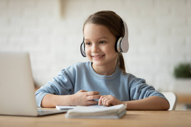 Little schoolgirl learning school subject distantly using pc and headphones Wearing wireless headphones makes videocall little beautiful schoolgirl using web cam and notebook learning school subject distantly due quarantine or home schooling. Remote self-education concept homeschooling photos stock pictures, royalty-free photos & images