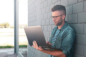 Young freelancer man using laptop in the street outdoors - Bearded handsome guy having fun typing and surfing online - Influencer or blogger working outdoors - Technology and fashion lifestyle concept