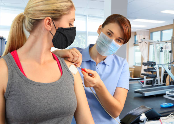 istock Physical Therapist Preparing Patient's Shoulder For Electrical Stimulation While Both Wear Protective Masks 1252962103