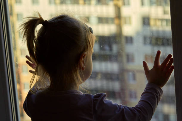 istock Girl looks lonely through window by putting her hands on window sill 1252965393