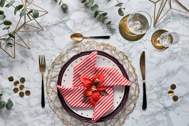istock Christmas table setting with red napkin, golden utensils and fresh eucalyptus leaves on white marble background. Flat lay, top view on table with golden cutlery, white plates and geometric hexagons. 1252967014