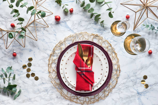 istock Christmas table setting with gold utensils in folded textile napkin and fresh eucalyptus on marble background. Flat lay on table with golden cutlery, white plates and geometric hexagons. 1252967035