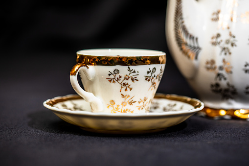Antique porcelain coffee cup on white background with reflection. Dishes with gold pattern. Table service.