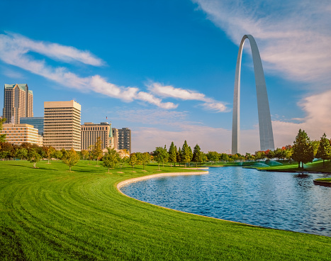 The Gateway Arch National Park is alive with autumn color and green evergreen trees surrounding the lake under the Arch.