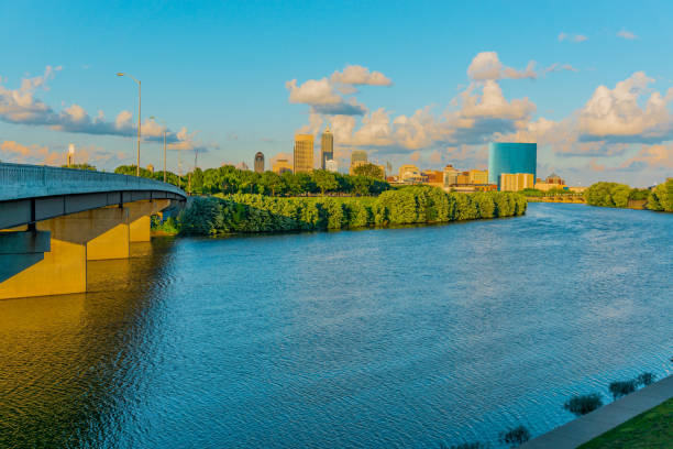 The White River and bridge lead to downtown Indianapolis in Indiana. The  White River flows just outside the skyline of Indianapolis, Indiana  and all glow in the last light of the day. landscape view of indianapolis indiana during the day stock pictures, royalty-free photos & images