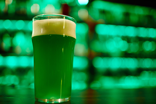 Glass of green foaming beer on background of contemporary pub interior