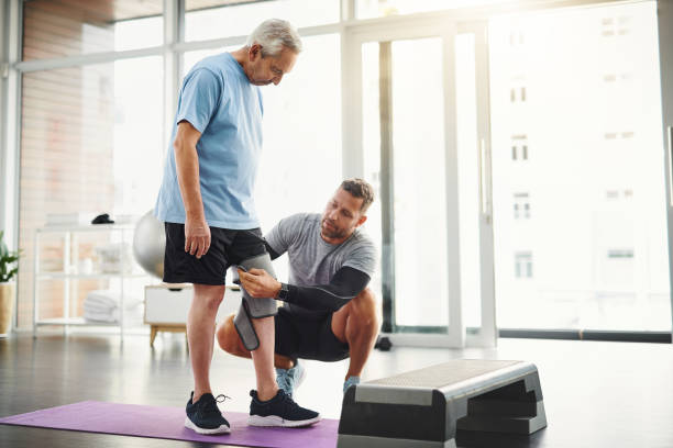 Let's get your body back to functioning 100% Shot of a young male physiotherapist assisting a senior patient in recovery knee brace stock pictures, royalty-free photos & images