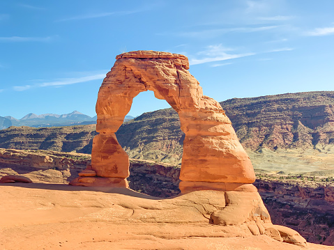 Amazing view of distant rock mountains view with a natural window through  the hole in a window on the walls of red clay rock. Desert noon with Delicate Arch in Arches National Park Utah