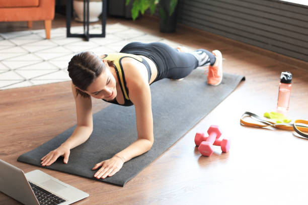 istock Fitness woman doing plank and watching online tutorials on laptop, training in living room. Stay at home activities. Top view. 1253012873