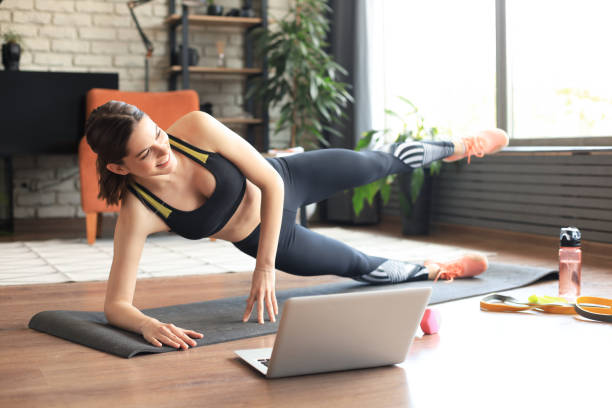 istock Fitness beautiful slim woman doing side plank and watching online tutorials on laptop, training in living room. Stay at home activities. 1253013008