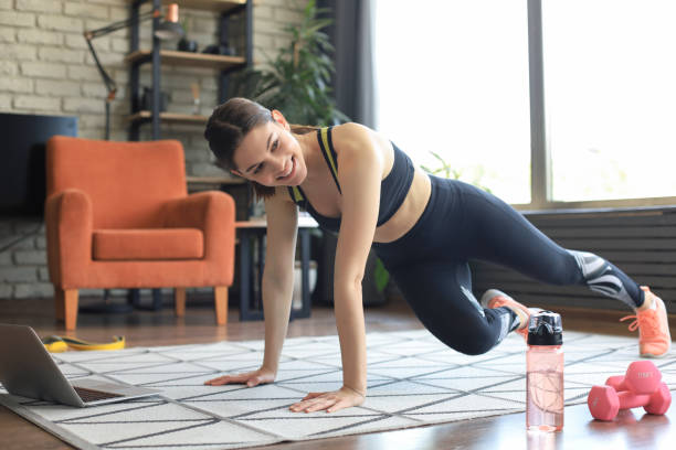 istock Beautiful fitness woman doing mountain climber exercises watching online tutorials on laptop, training in living room. Healthy lifestyle. Girl goes in for sports at home. 1253013042