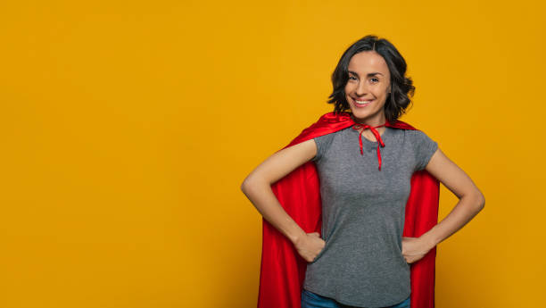 i am a superwoman! a young, beautiful girl, standing confidently with her fists on her waist, wearing red superman cloak, smiling like a real hero, ready to accomplish any task in the world. - real world imagens e fotografias de stock