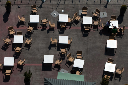 Outdoor restaurant. Empty tables and chairs. Only 2 people unrecognizable. Panoramic image with a multitude of unaligned objects.