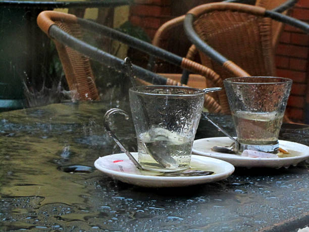 テラスバーでのシーン。コーヒーカップと皿が付くテーブルの上に雨滴が大きく飛び散る。雨の概念、雨の日、計画の変更、逃げるための背景画像。大洪水による空のテラス。 - when it rains it pours ストックフォトと画像