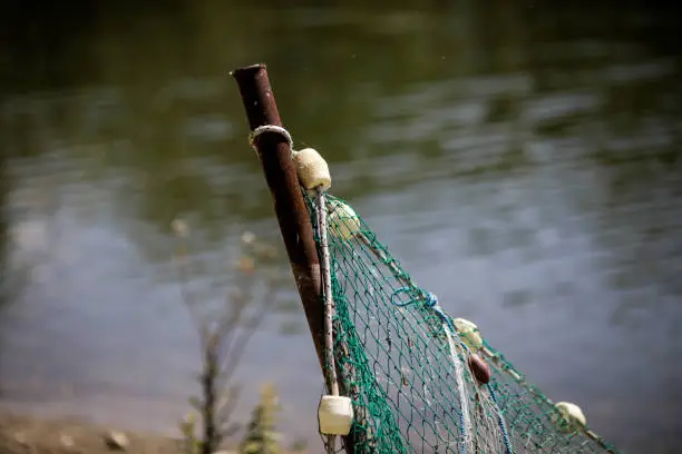 Details with a fishing net tied to a metal post on a river bank.