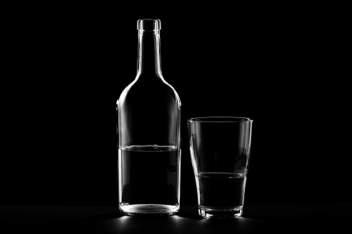 A single dirty vintage perfume bottle on a reflective black background with copy space.