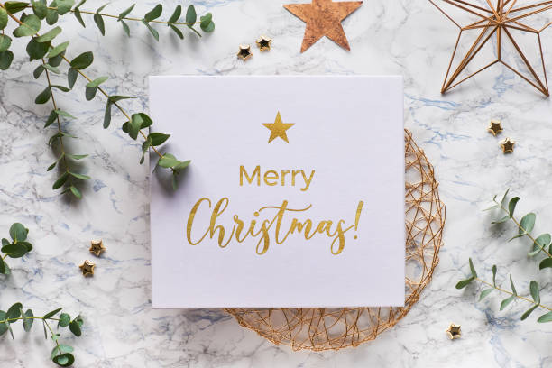 istock Christmas frame with fresh eucalyptus twigs and golden geometric decorations - hexagons, trinkets and wire shapes. Flat lay, top view on white marble background with text Merry Christmas in gold. 1253023829