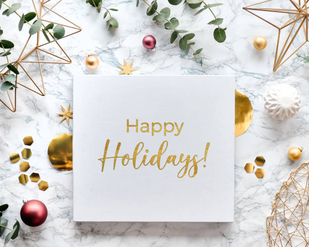 Light Christmas frame with fresh eucalyptus twigs and golden geometric decorations - hexagons, trinkets and wire shapes. Flat lay on white marble background with text Happy Holidays in golden text.