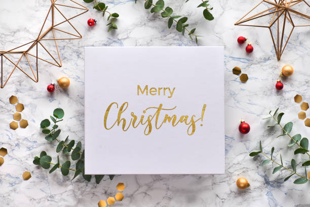 istock Christmas frame with fresh eucalyptus twigs and golden geometric decorations - hexagons, trinkets and wire shapes. Flat lay, top view on white marble background with text Merry Christmas in gold. 1253023890