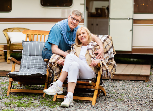 Mature family resting on deck chairs near their camper van in countryside