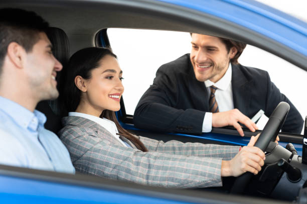 istock Happy Couple Testing Car With Dealer Sitting In Auto 1253024155
