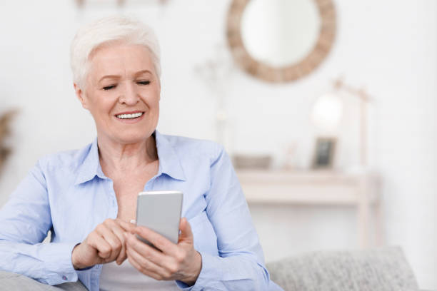 istock Smiling elderly woman holding cellphone, reading news while resting at home 1253024780
