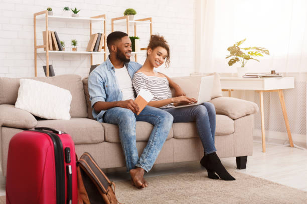 istock Black Couple Using Laptop Sitting With Travel Suitcase At Home 1253024984